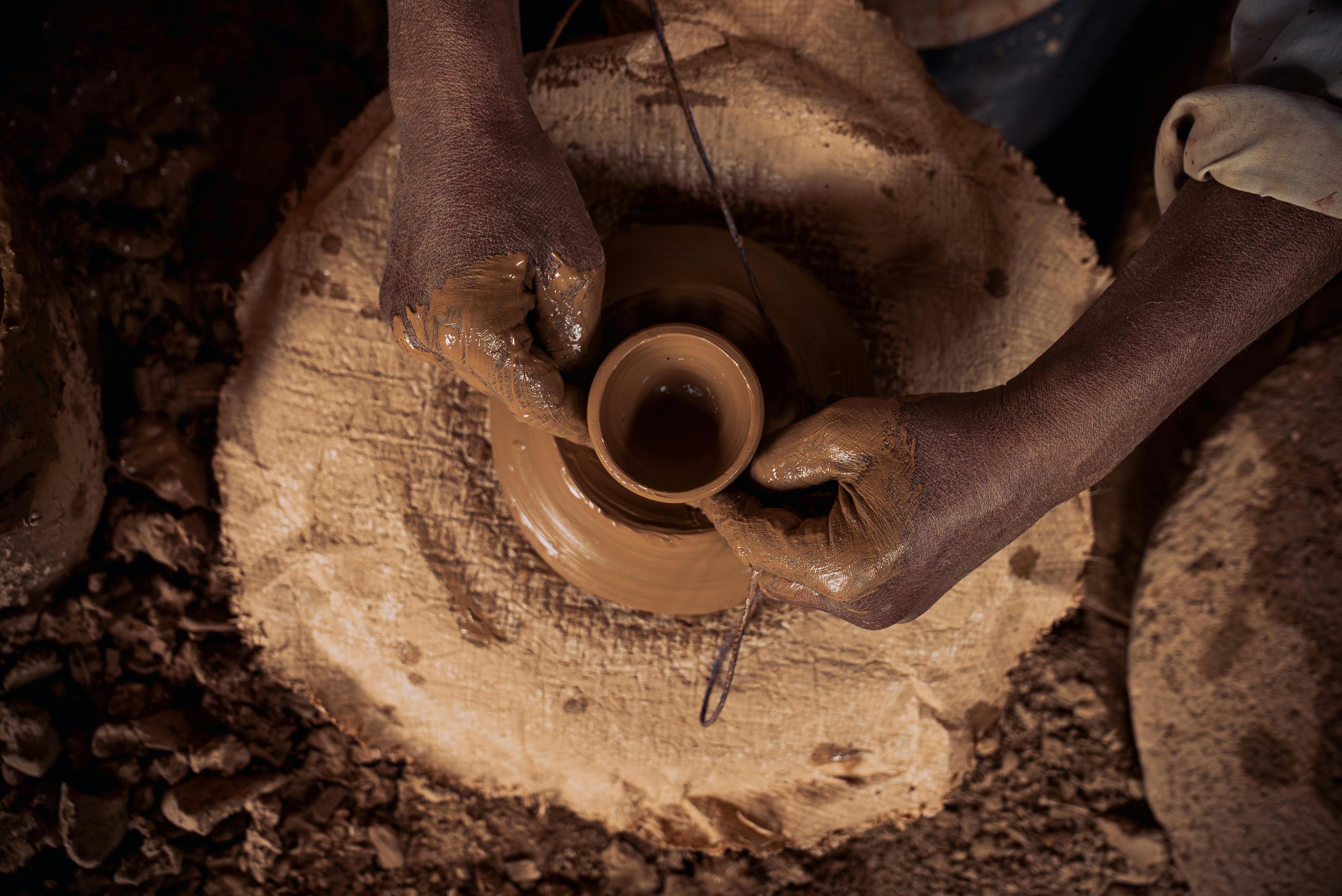 Mani che modellano una ciotolina su un tornio rustico coperto di polvere d'argilla, laboratorio di ceramica a Marrakech