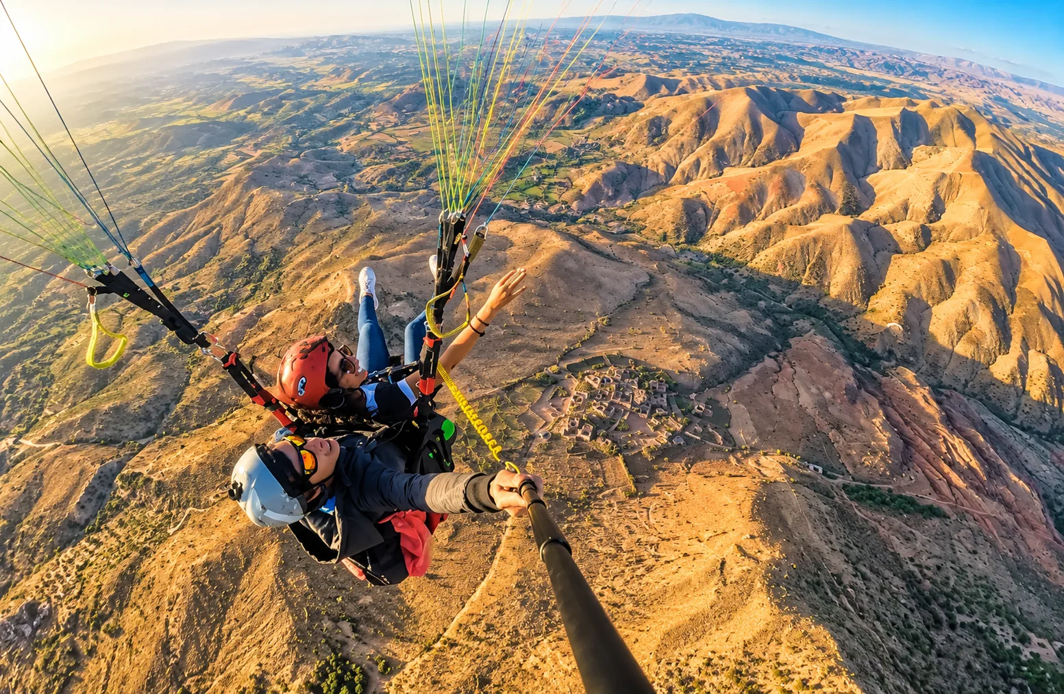 Pilota e passeggero in tandem che si fanno un selfie in volo sopra creste ocra, parapendio vicino a Marrakech