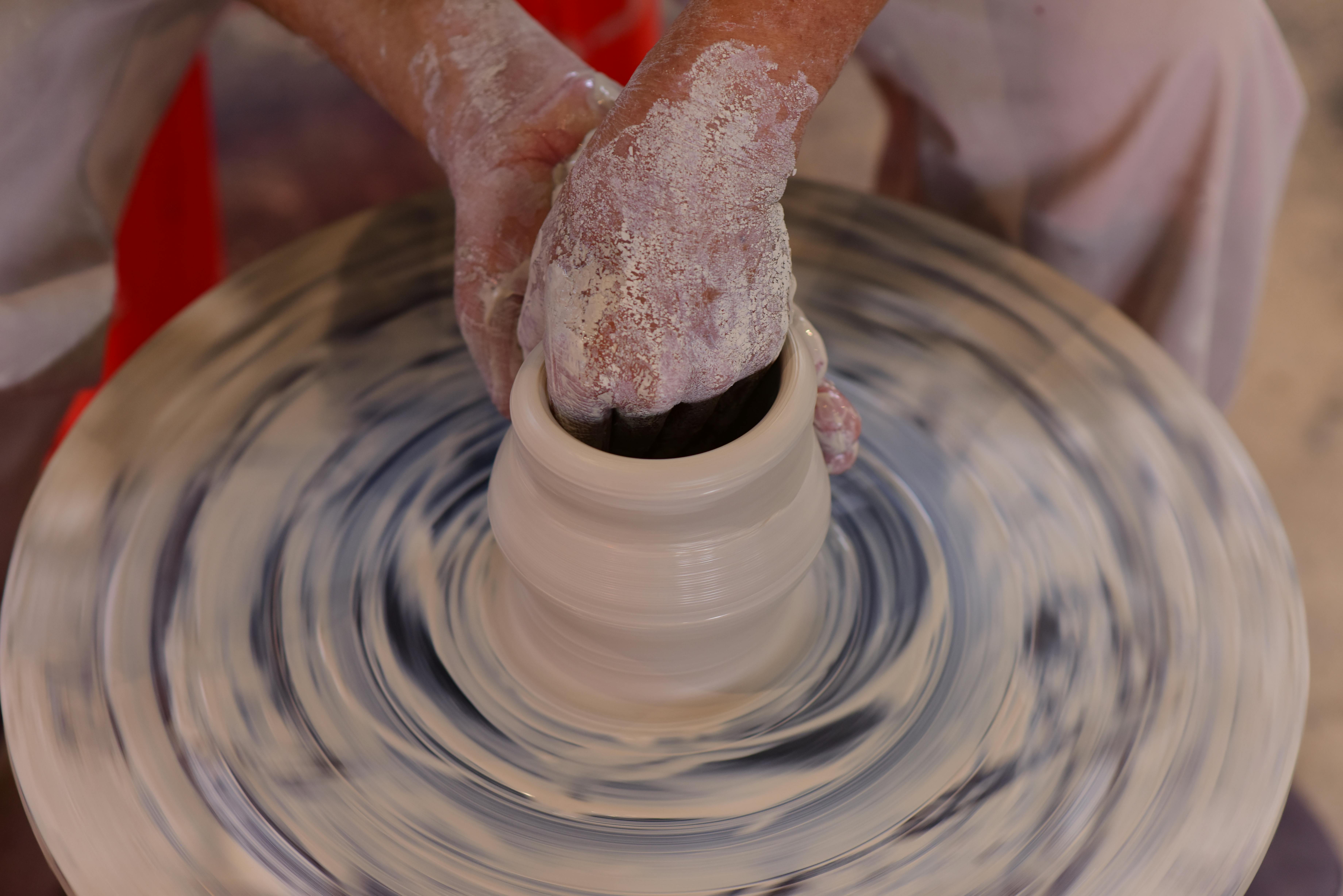 Mani che alzano la parete di un vaso di argilla bianca sul tornio, corso di ceramica a Marrakech