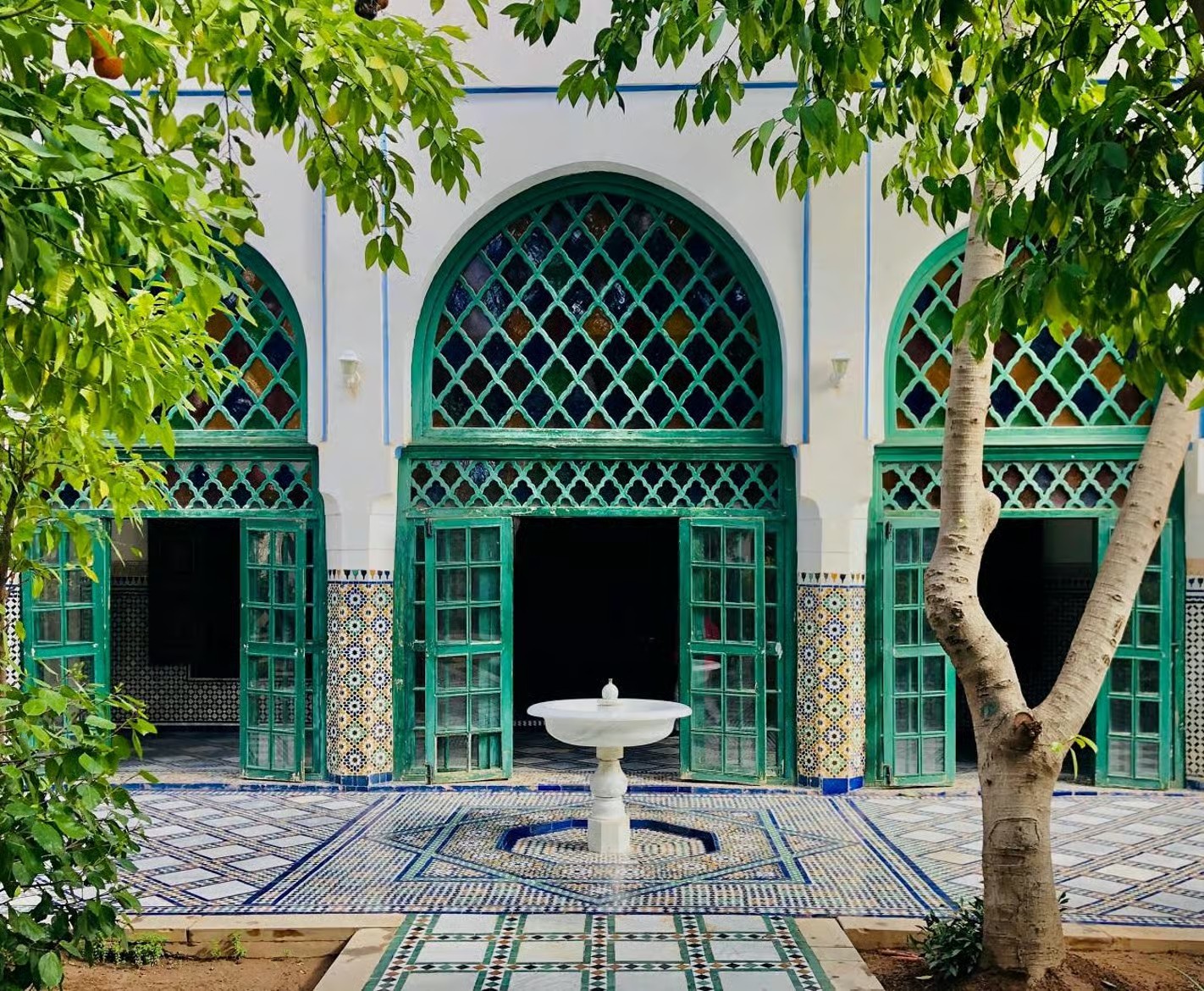 Green carved wooden doors and arches around a white fountain in a palace patio, Marrakech guided tour