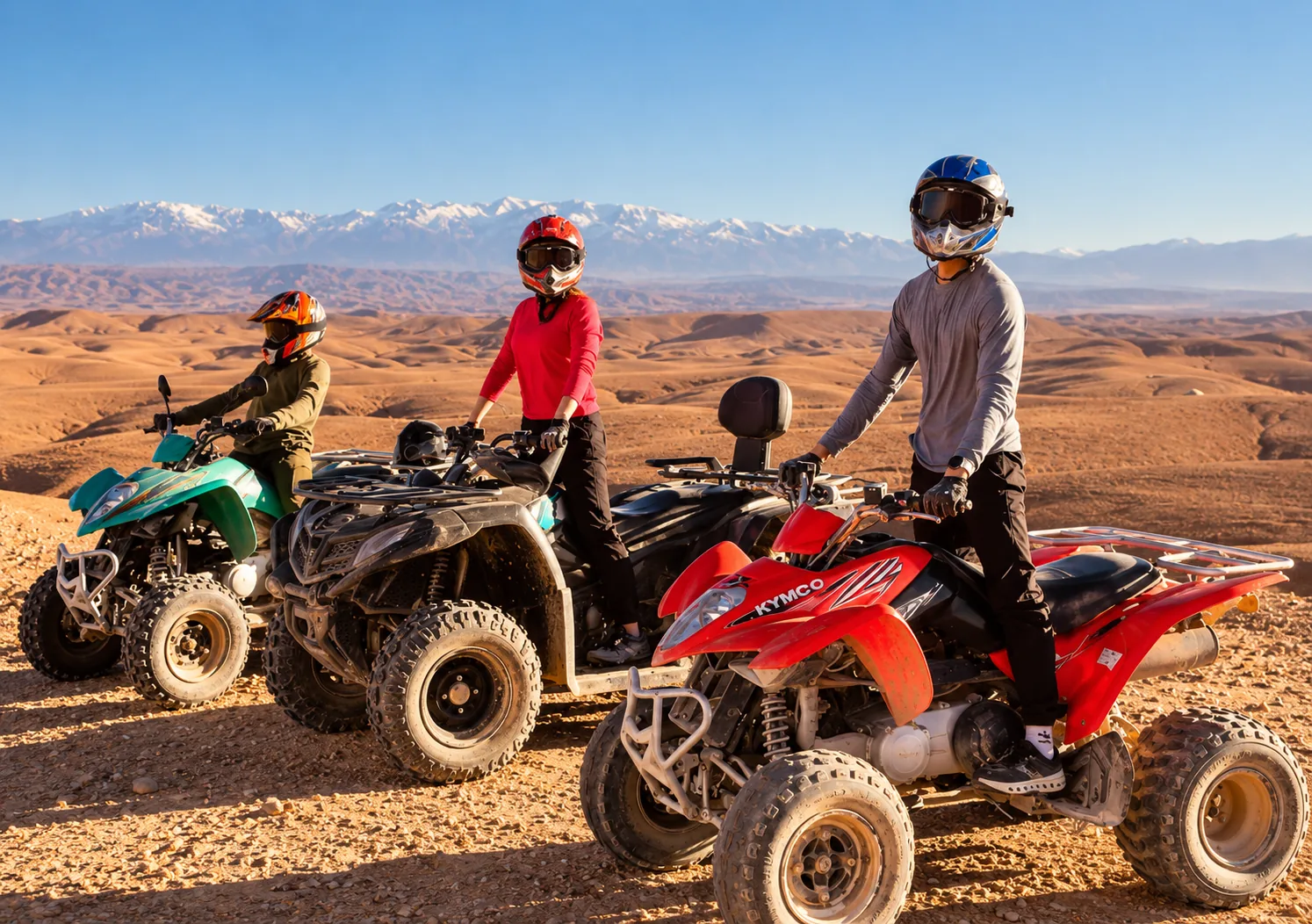 Three riders on red, black and green quads during quad biking in the Agafay desert, snowy Atlas peaks behind