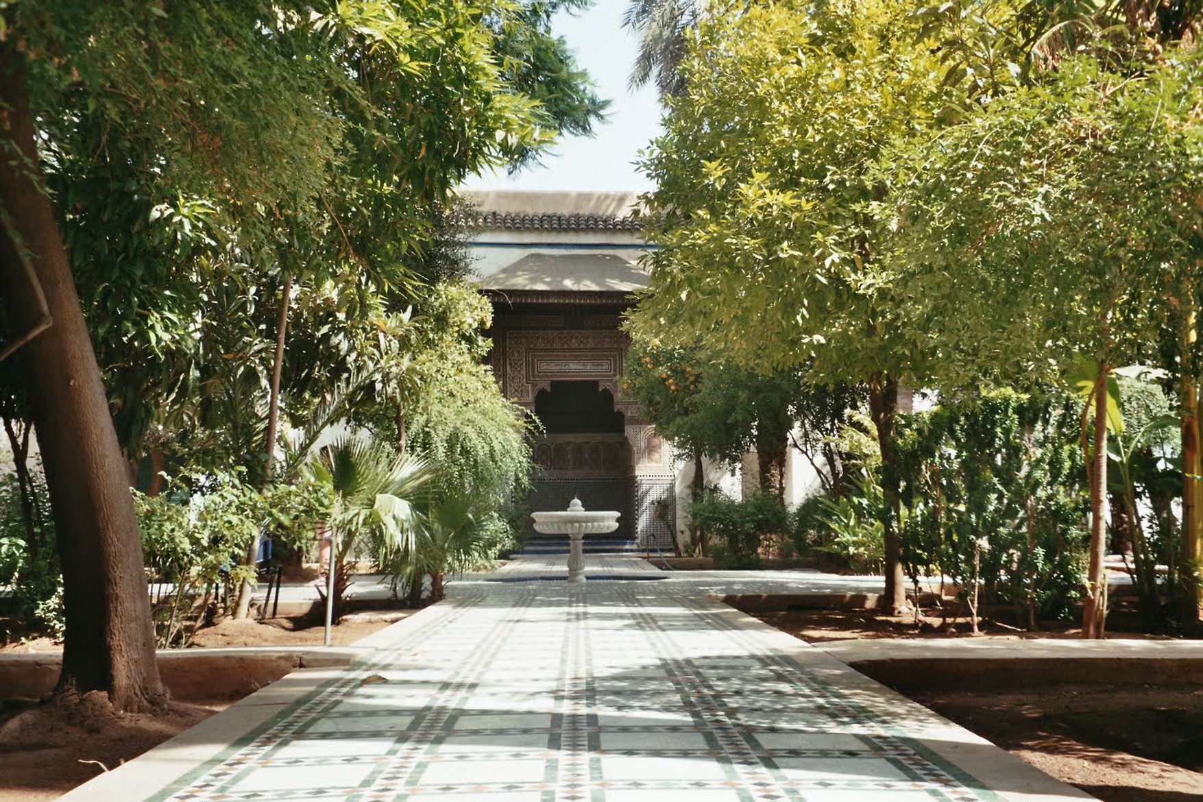 Shaded tiled path through a garden of trees leading to a palace fountain, on a guided tour of Marrakech
