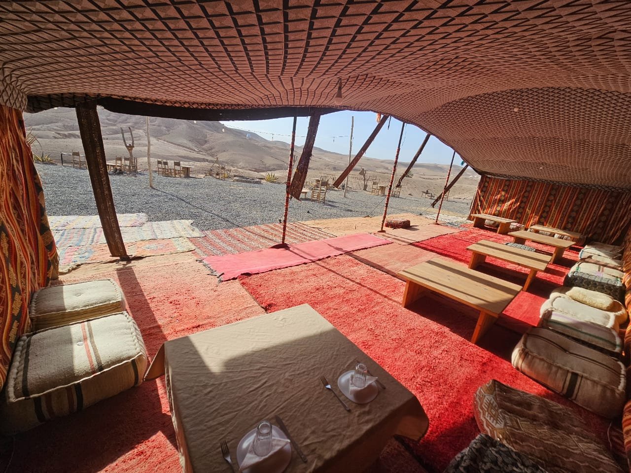 Dining tent with low tables and woven rugs at Boujemaa Agafay camp