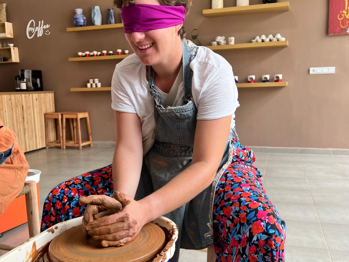 Partecipante bendata che ride mentre centra l'argilla sul tornio, corso di ceramica a Marrakech
