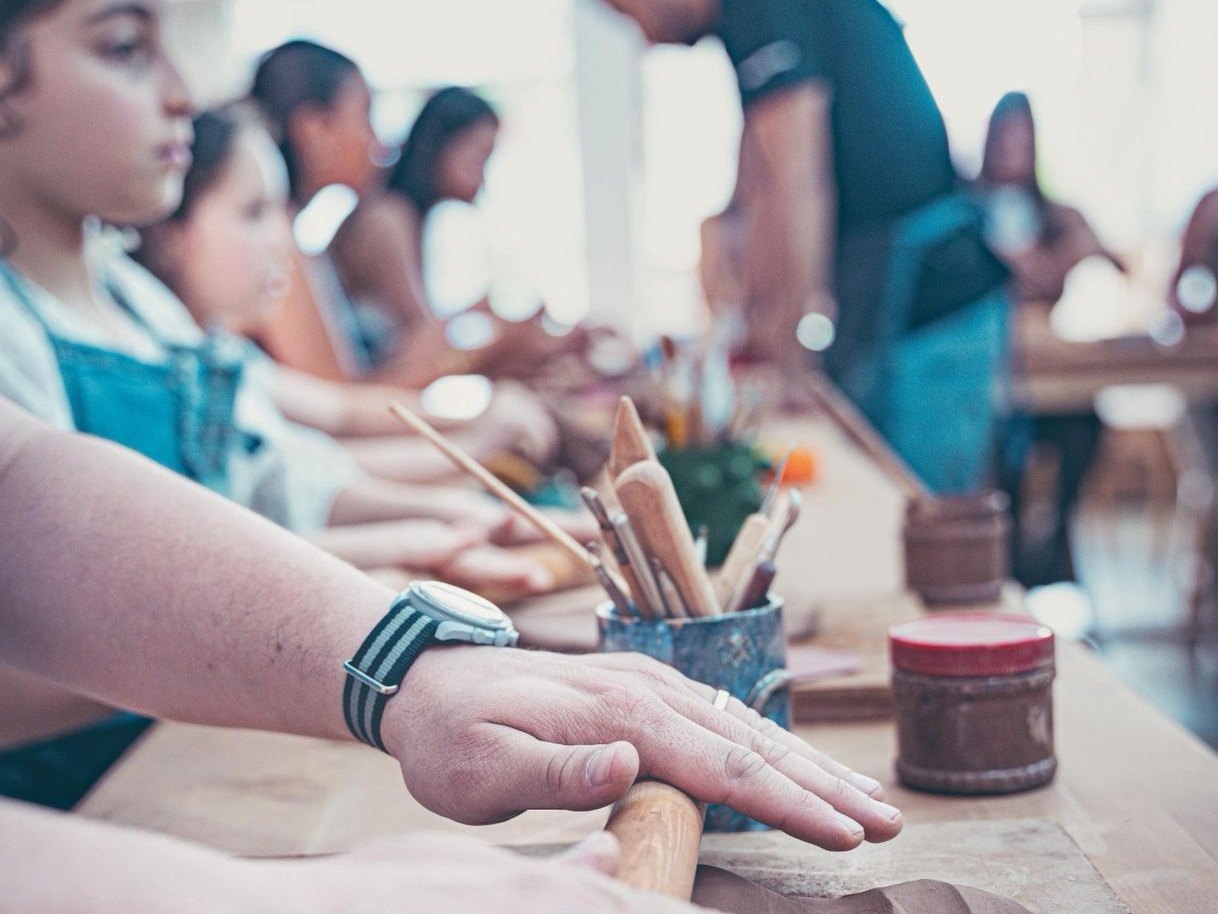 Bambini e adulti che stendono l'argilla con mattarelli di legno a un lungo tavolo, corso di ceramica per famiglie a Marrakech