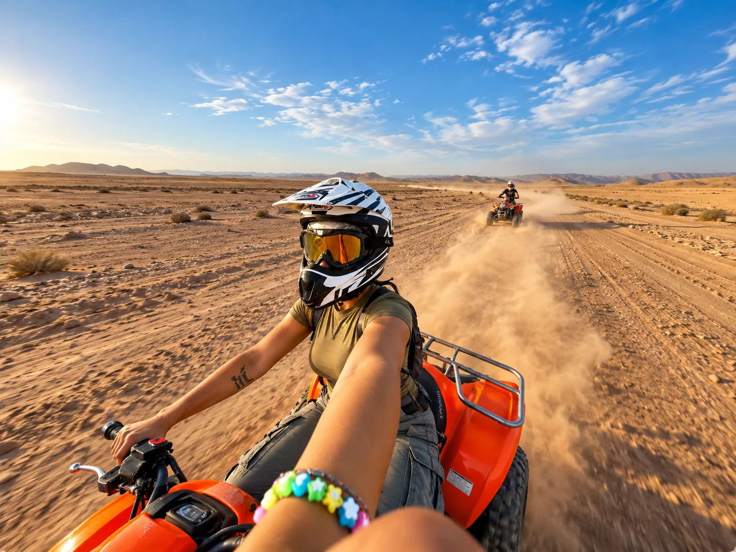 Rider's view from an orange quad of a helmeted driver on a dusty track, quad biking in the Agafay desert