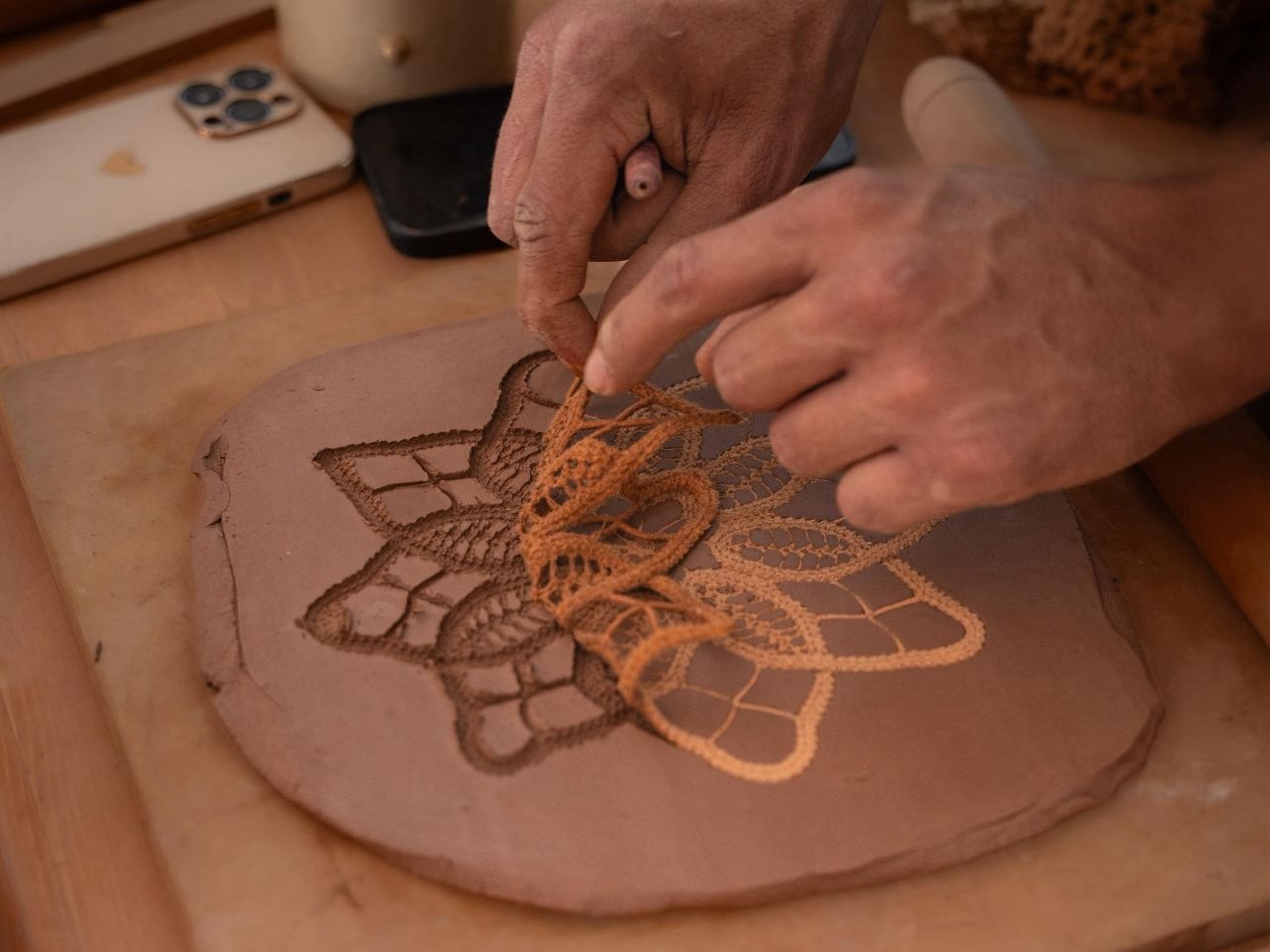 Mani che premono uno stencil di pizzo su una lastra d'argilla per stampare un motivo floreale, corso di ceramica a Marrakech