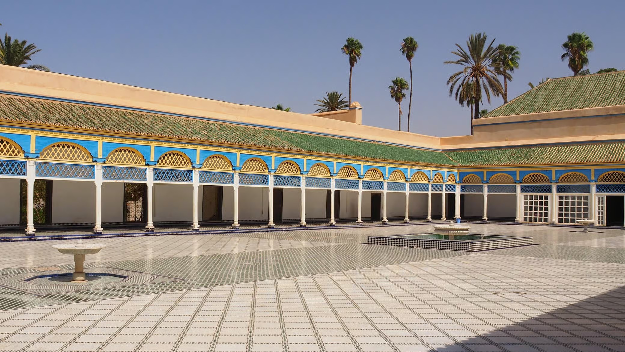 Empty marble courtyard of Bahia Palace with blue and yellow painted galleries, Marrakech guided tour