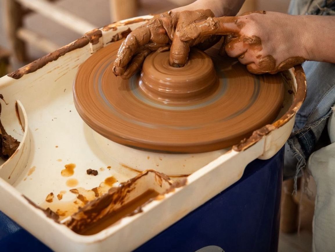 Mani coperte d'argilla che centrano un blocco d'argilla sul tornio, corso di ceramica a Marrakech