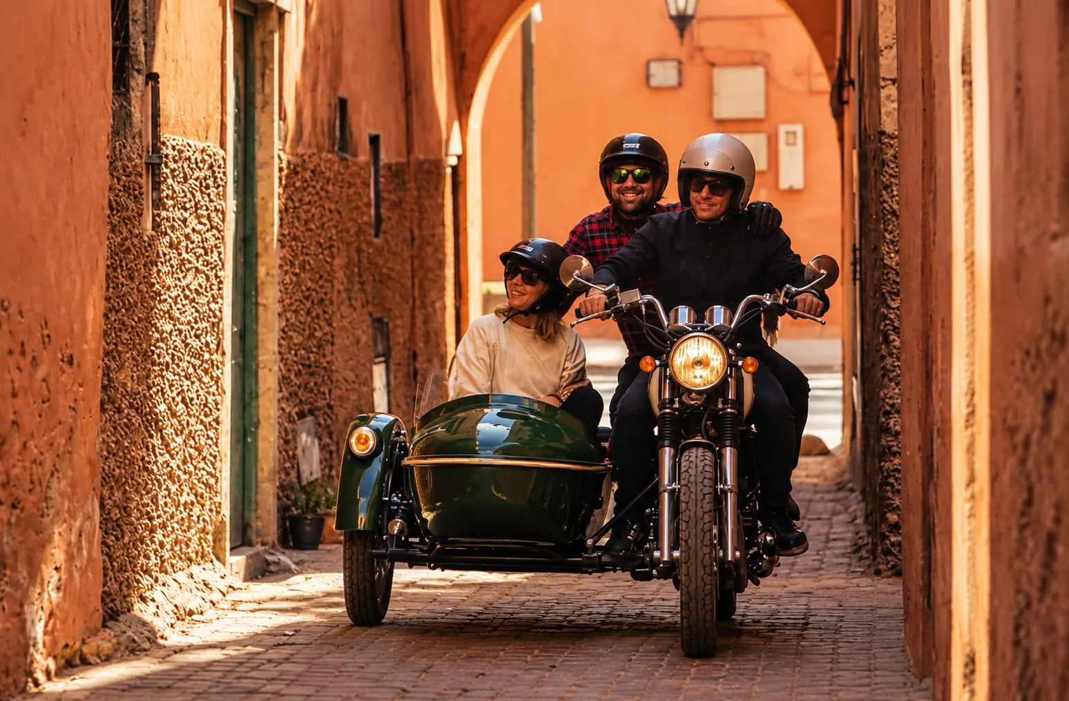Couple in helmets riding a green side-car through a narrow terracotta alley, side-car tour in Marrakech