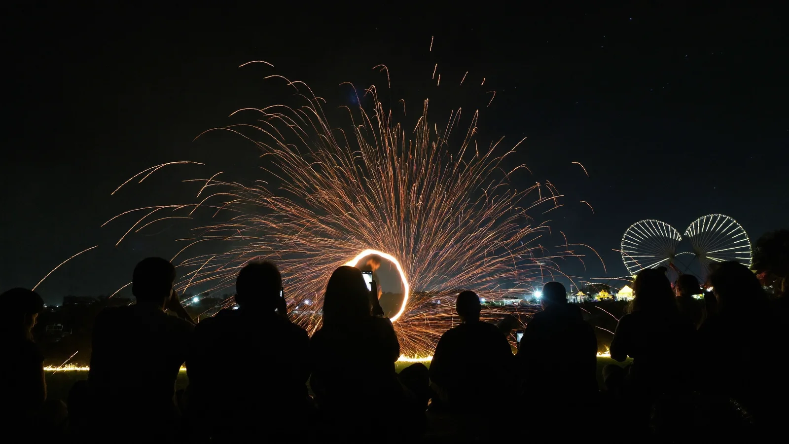 Silhouetten von Zuschauern, ein Feuerkünstler zieht nachts Funkenkreise, Quad- und Paintball-Pack in Marrakech