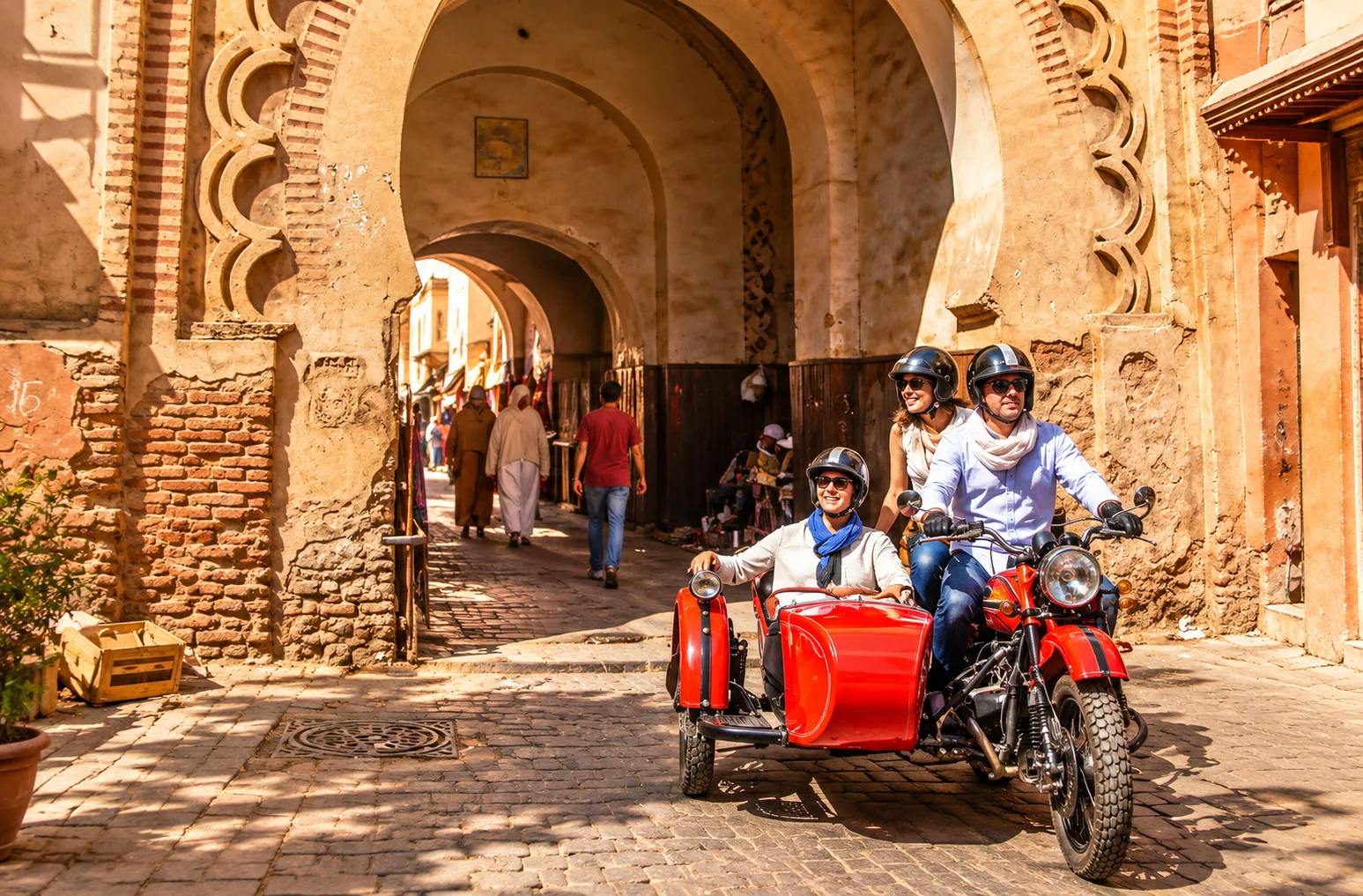 Smiling couple in a red side-car coming through a carved medina gate, side-car tour in Marrakech
