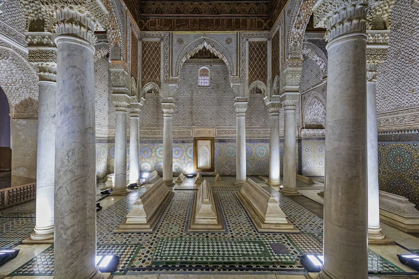 Marble columns and carved stucco over tiled tombs in a historic mausoleum hall, Marrakech heritage visit