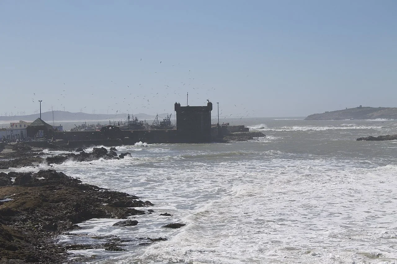 Raue See und schwarze Felsen, in der Ferne der Hafenturm und Möwen, Tagesausflug nach Essaouira