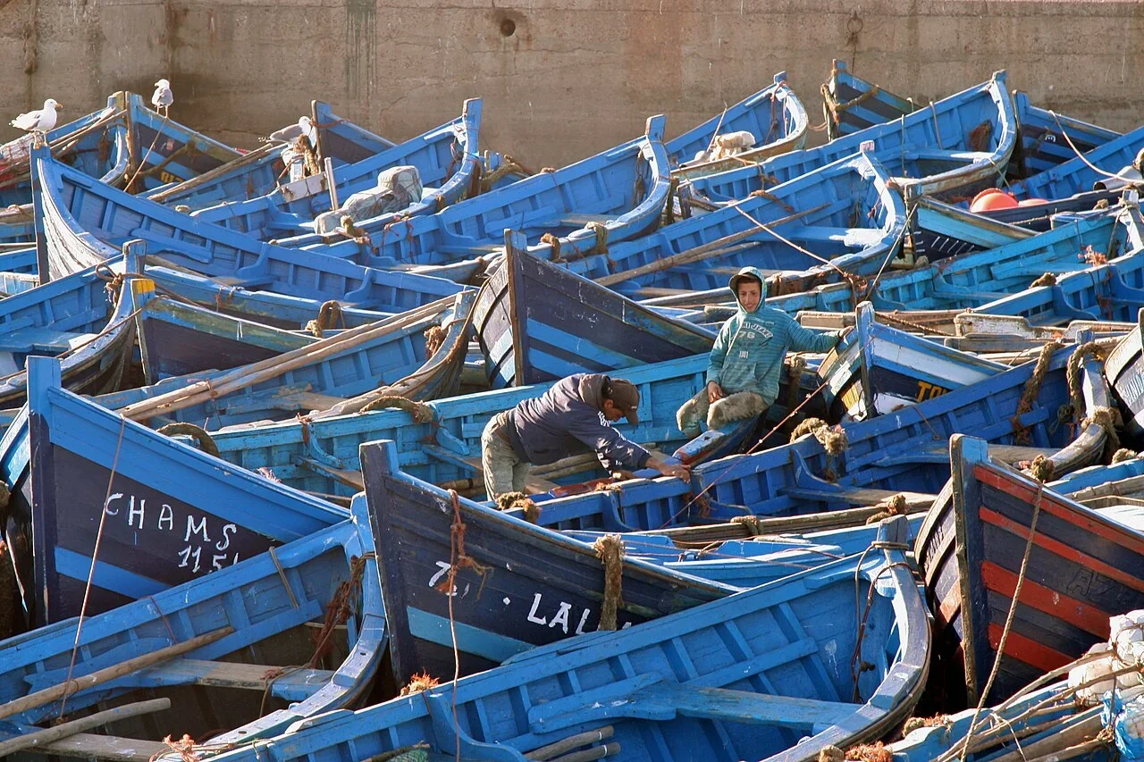 Fischer reparieren ihre Ausrüstung zwischen dicht gedrängten blauen Holzbooten im Hafen, Tagesausflug nach Essaouira