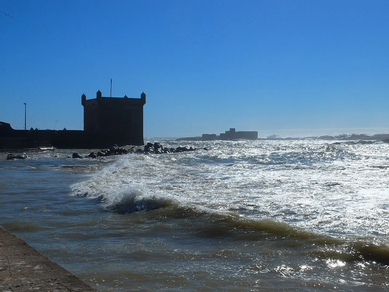 Atlantikwellen brechen an den Felsen vor dem befestigten Hafenturm, Tagesausflug nach Essaouira ab Marrakech