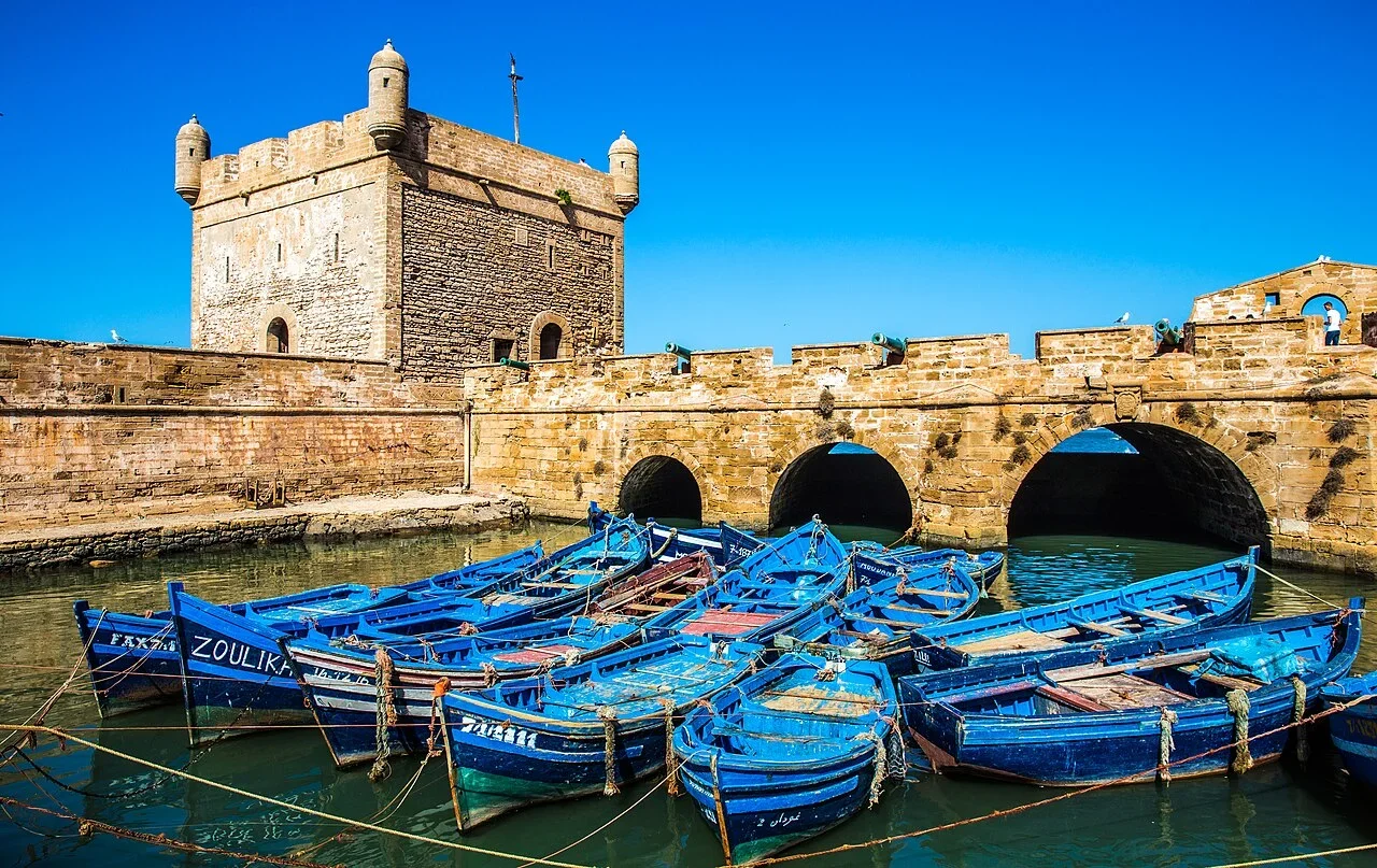 Blaue Boote unter der gewölbten steinernen Hafenmauer und dem Bastionsturm, Tagesausflug nach Essaouira ab Marrakech