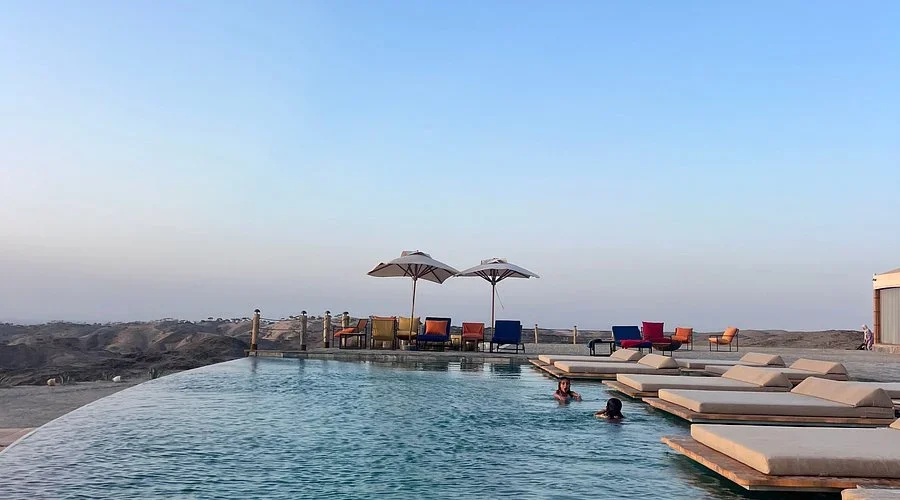 Schwimmer im Infinity-Pool, Liegen und Schirme auf dem Deck mit Blick auf die Hügel, Seven Saints Agafay Pool-Tag