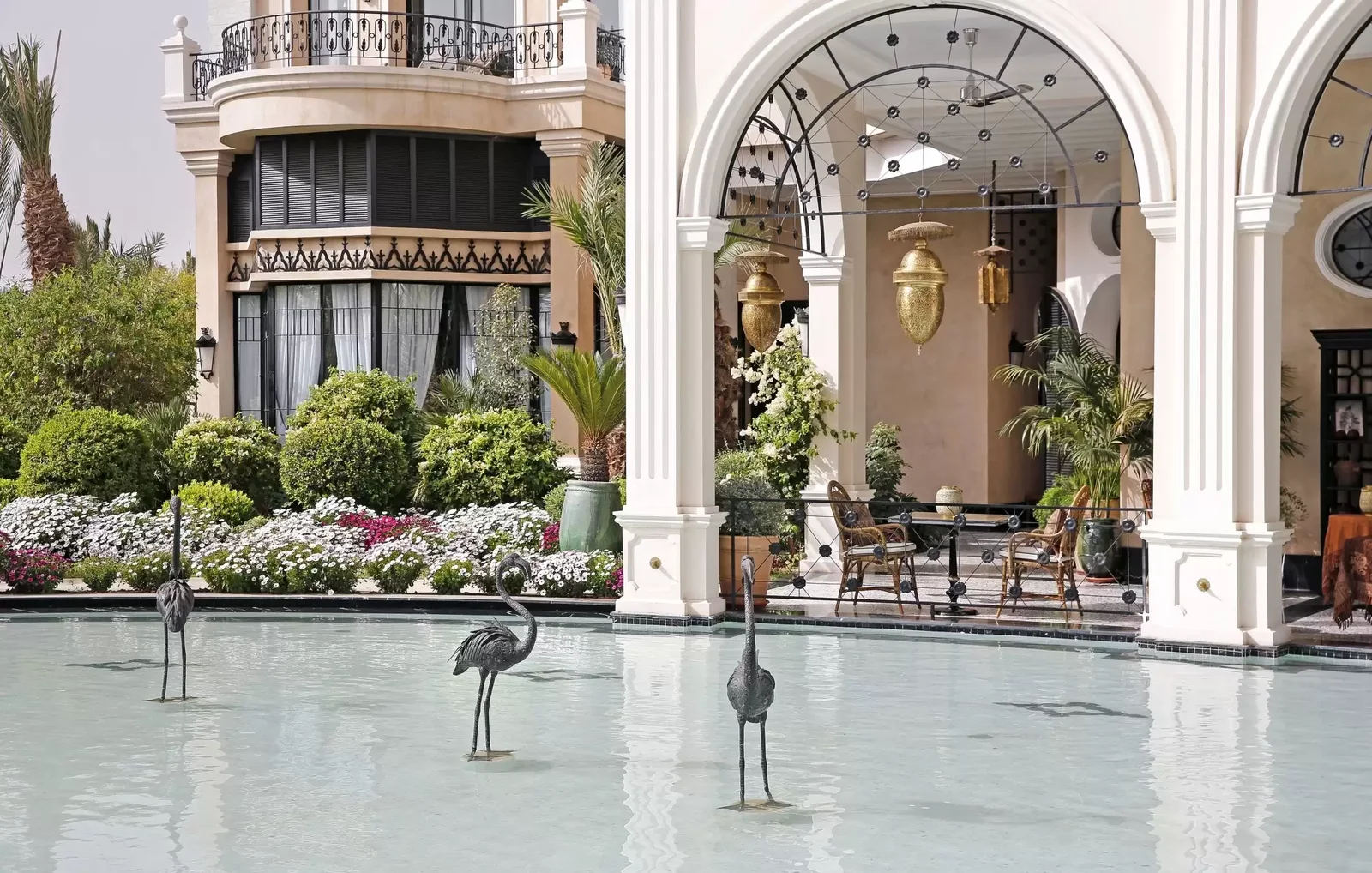 Reiherstatuen in einem flachen Becken vor weißen Bögen und Blumenbeeten, Palais Ronsard Pool-Tagespass