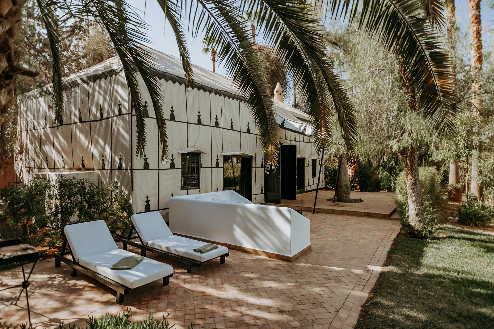 Gartenterrasse mit Liegen an einer weißen Zinnenmauer und Palmen, Palais Rhoul Pool-Tagespass in der Palmeraie