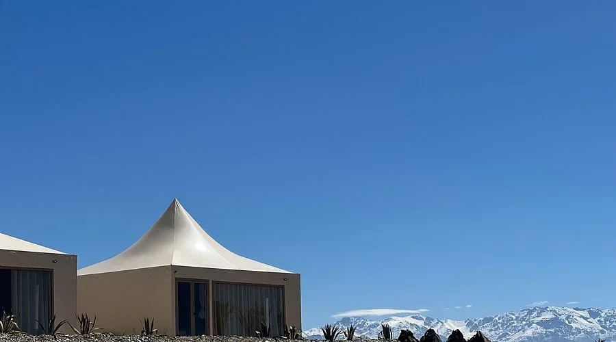 Weiße Spitzzelt-Lodge unter klarem Himmel, am Horizont verschneite Atlasgipfel, Seven Saints Agafay Pool-Tagespass